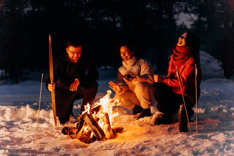 Friends enjoying a cozy bonfire in the snow during a chilly winter evening.