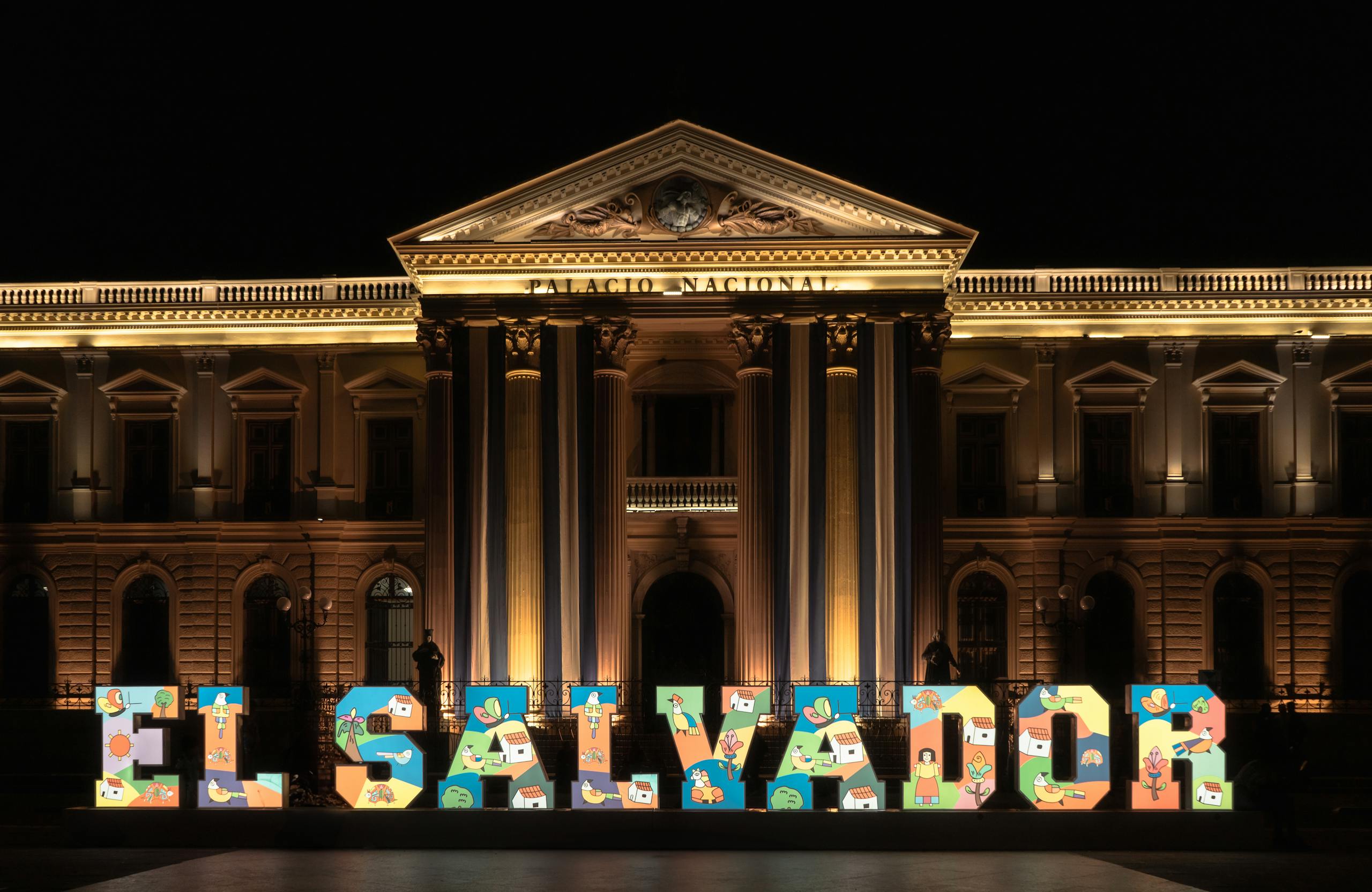 Front view of the illuminated Palacio Nacional in San Salvador at night with vibrant El Salvador sign.